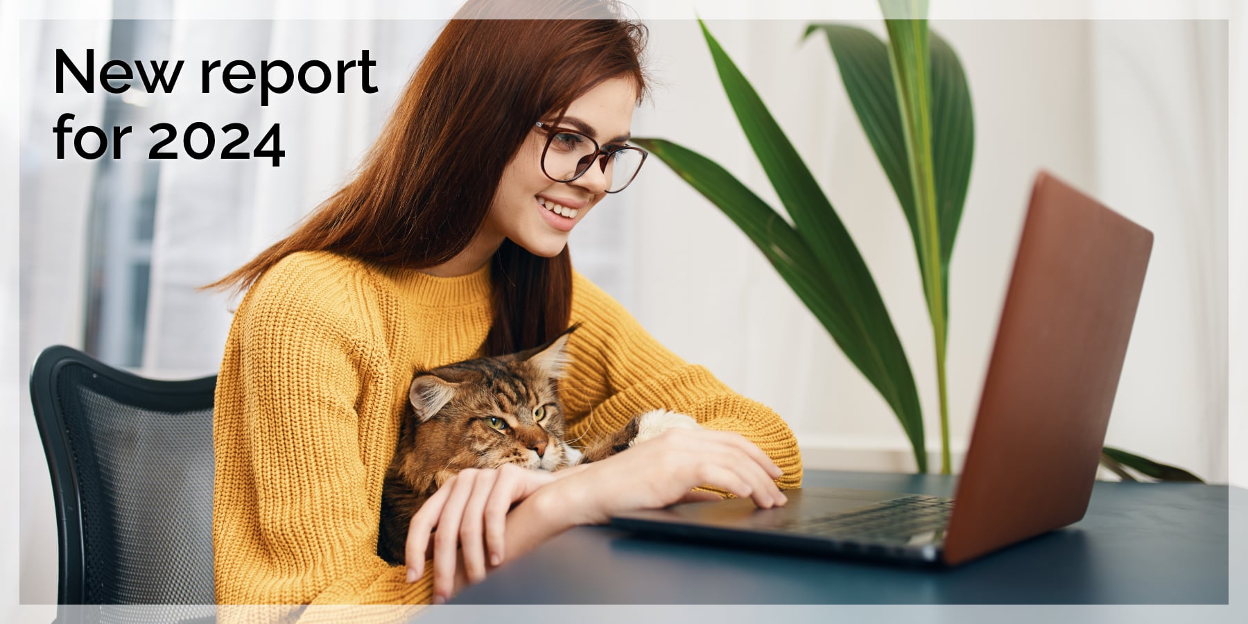 A young woman in a warm yellow sweater works on a laptop while holding her cat.