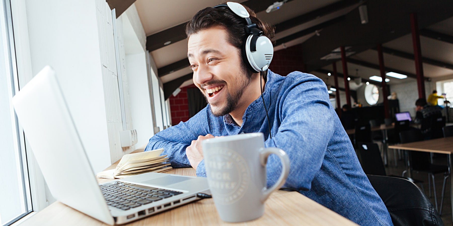 Very happy man in headphones talking to on his laptop.