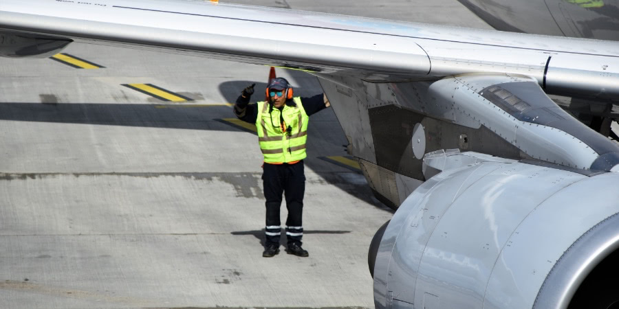 Ground crew in high-viz vest, next to a plane on the runway.