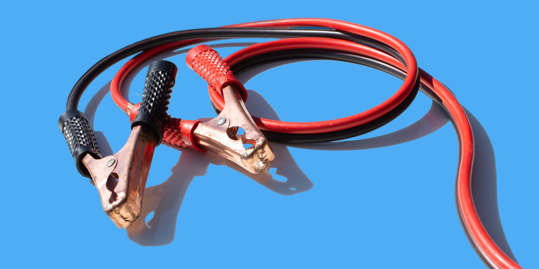 Jumper cables, big electrical clips that you would clip to a car battery to 'jump start' it. Red and bacl cables, on a blue background.