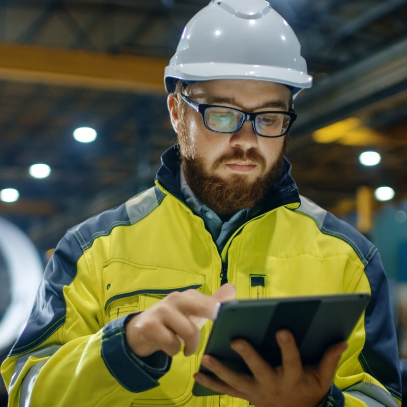 Bearded chap in a hard hat and high viz yellow jacket using a tablet