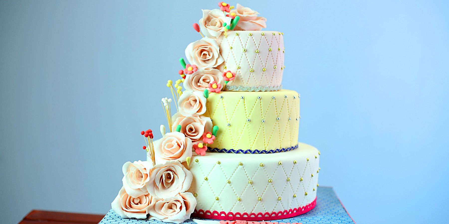 Three tiered wedding cake in yellow and green with a cascade of roses.